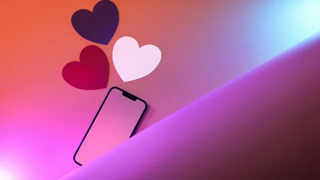 Smartphone mit drei Papierherzen auf pink-violettem Hintergrund – Tinder oder Lovoo im Vergleich