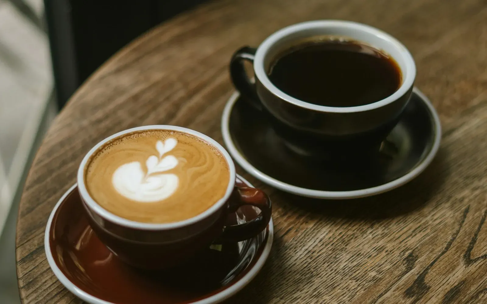 Zwei Kaffeetassen mit Latte Art auf einem runden Holztisch im Café – Anzeichen für Interesse beim Date