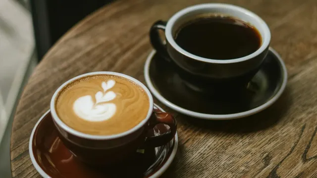 Zwei Kaffeetassen mit Latte Art auf einem runden Holztisch im Café – Anzeichen für Interesse beim Date